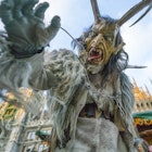 A person dressed as Krampus, the Christmas demon, reaches for the camera while exposing a large tongue and pointy teeth. The Krampus costume also features two large horns protruding from the head and a hairy body